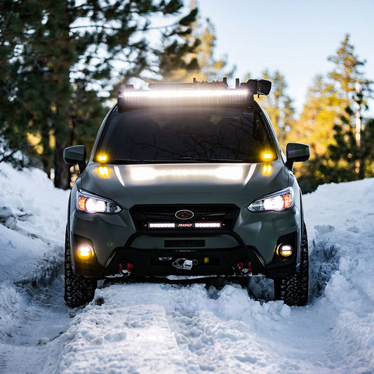 Green Subaru with Rigid LED light bar and fog lights driving through snow, off-road lighting setup