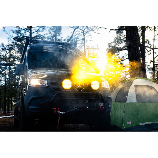 Black Mercedes van with bright LED lights parked beside green tent in forest at sunset