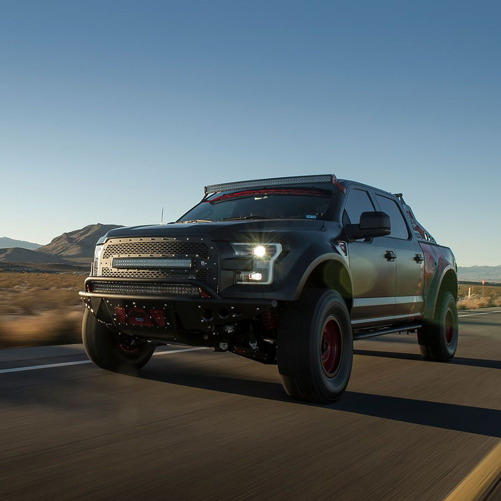 Custom lifted truck with off-road lights and rugged grille driving on desert highway