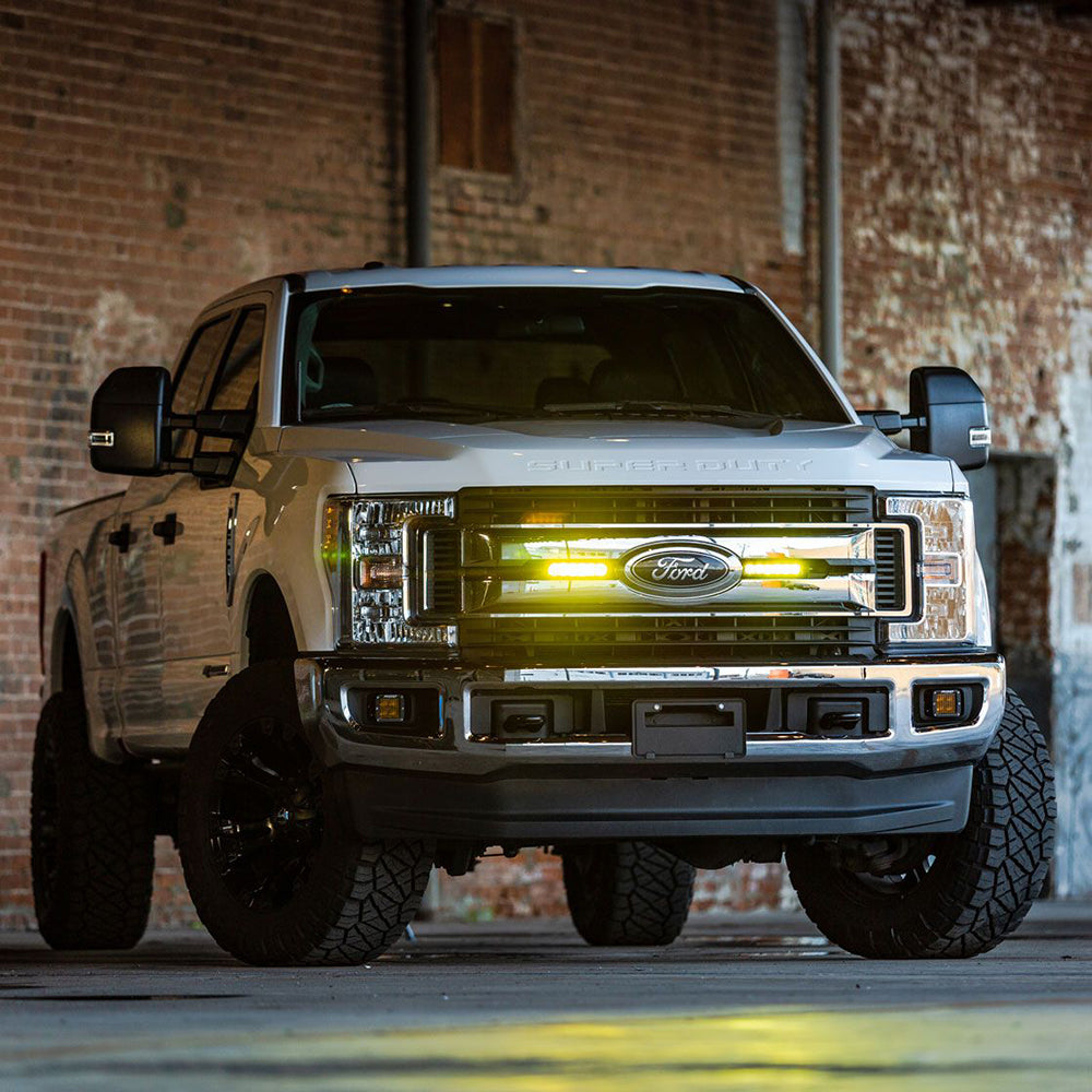 White Ford Super Duty truck with custom LED lighting, lifted suspension, and off-road tires in industrial setting